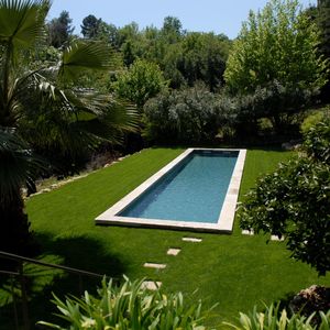 Piscine en forme de bassin de nage traditionnel équipé d'une belle margelle en pierre naturelle et d'un liner gris ardoise au milieu d'un gazon verdoyant.